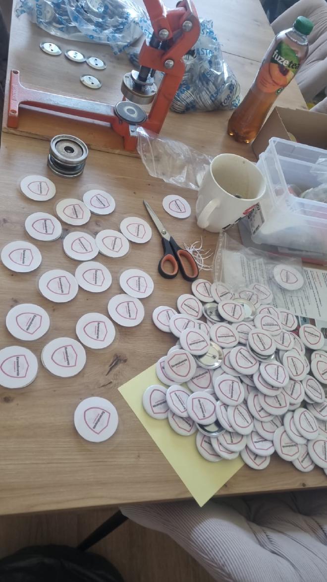 Eine Werkbank mit einer Buttonmaschine und vielen ausgeschnittenen und fertigen Jecke Freunde Buttons